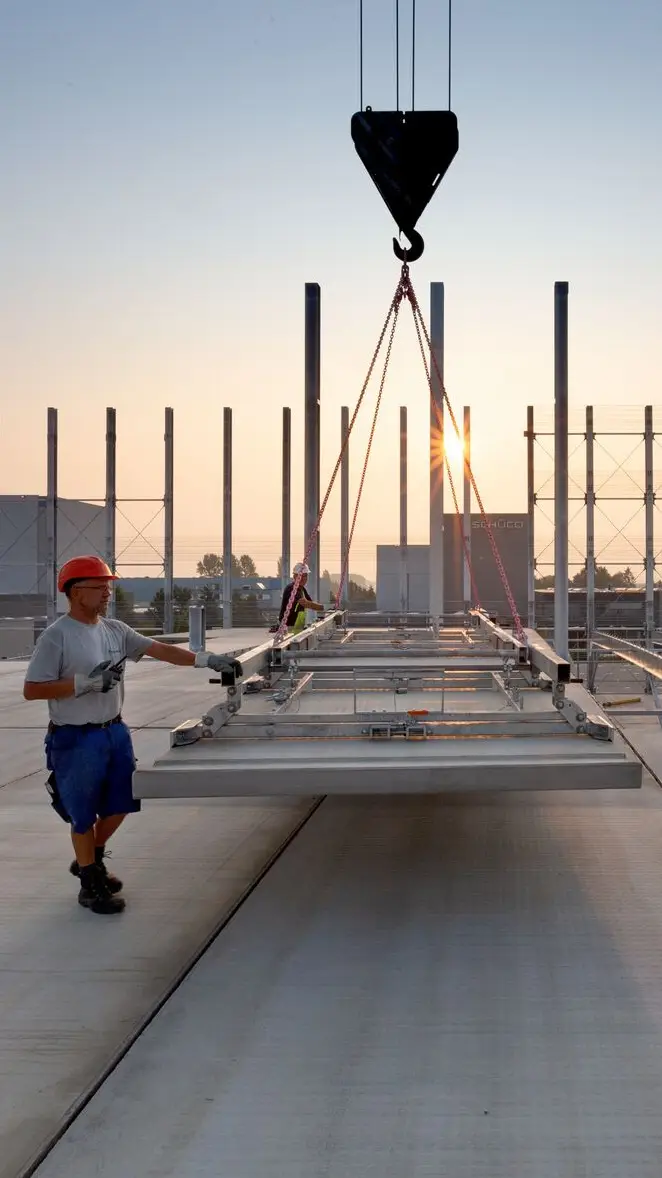 Worker with helmet during the assembly process of a steel element on a construction site at sunset.